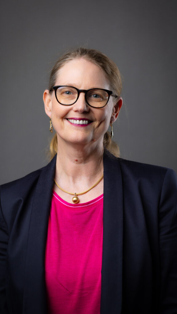 Lächelnde, blonde Frau mit Brille und im geschäftlichen Outfit