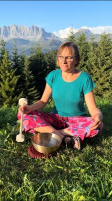 Frau mittleren Alters sitzt draussen im Schneidersitz in der Natur mit einer grossen Klangschale für mehr innere Klarheit