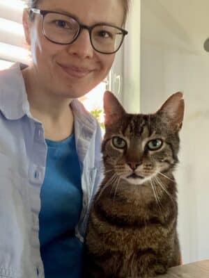 Junge Frau mit Brille und einer getigerten Katze auf dem Schoss