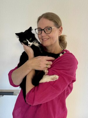 Frau mittleren Alters und Brille hält eine schwarz weisse Katze auf dem Arm